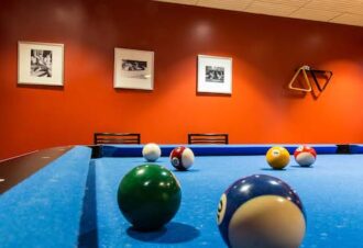 Close up of pool blue pool table looking at the bblack and white picture frames on an orange wall
